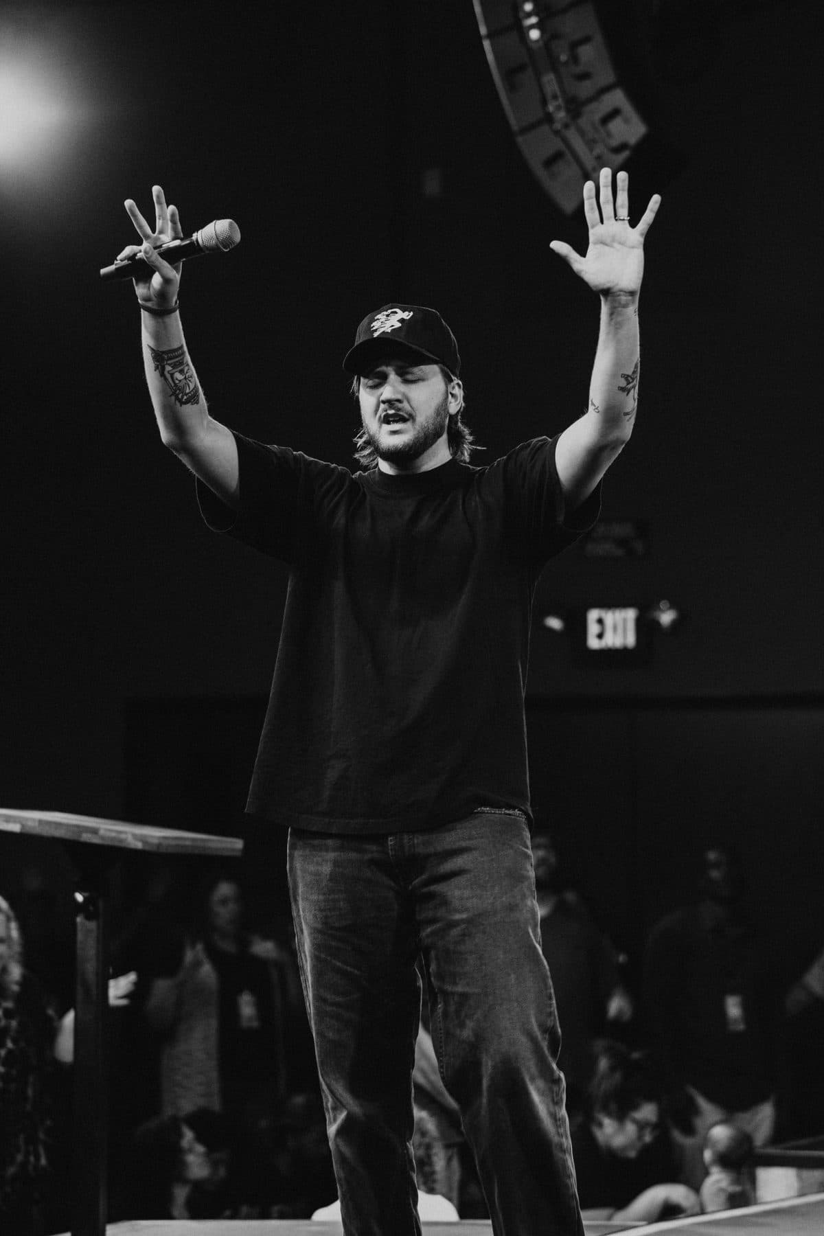 Chase on stage with both hands raised, a microphone in one, the room in worship behind him