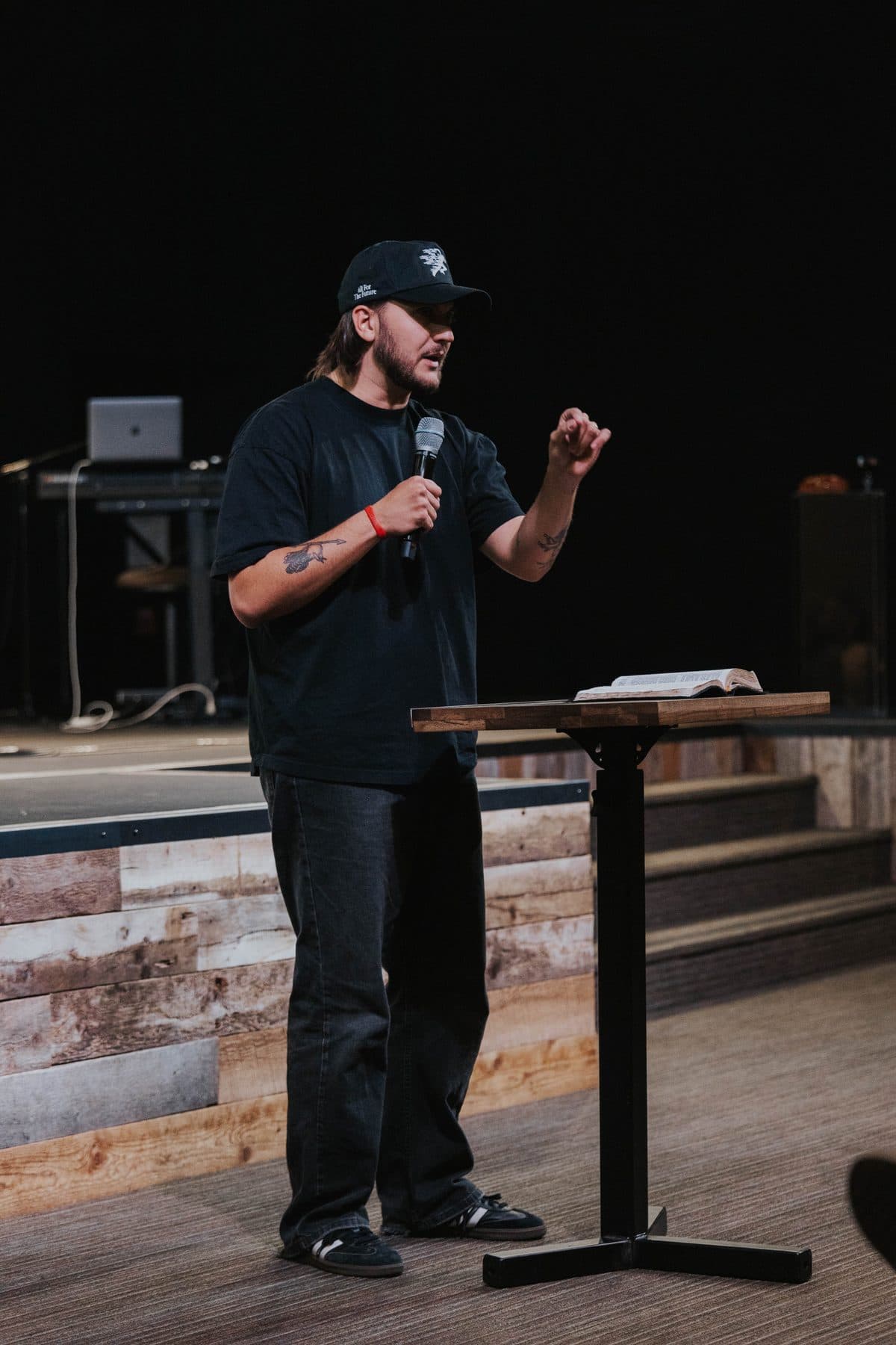 Chase preaching with a microphone beside a wooden pulpit, an open Bible on it